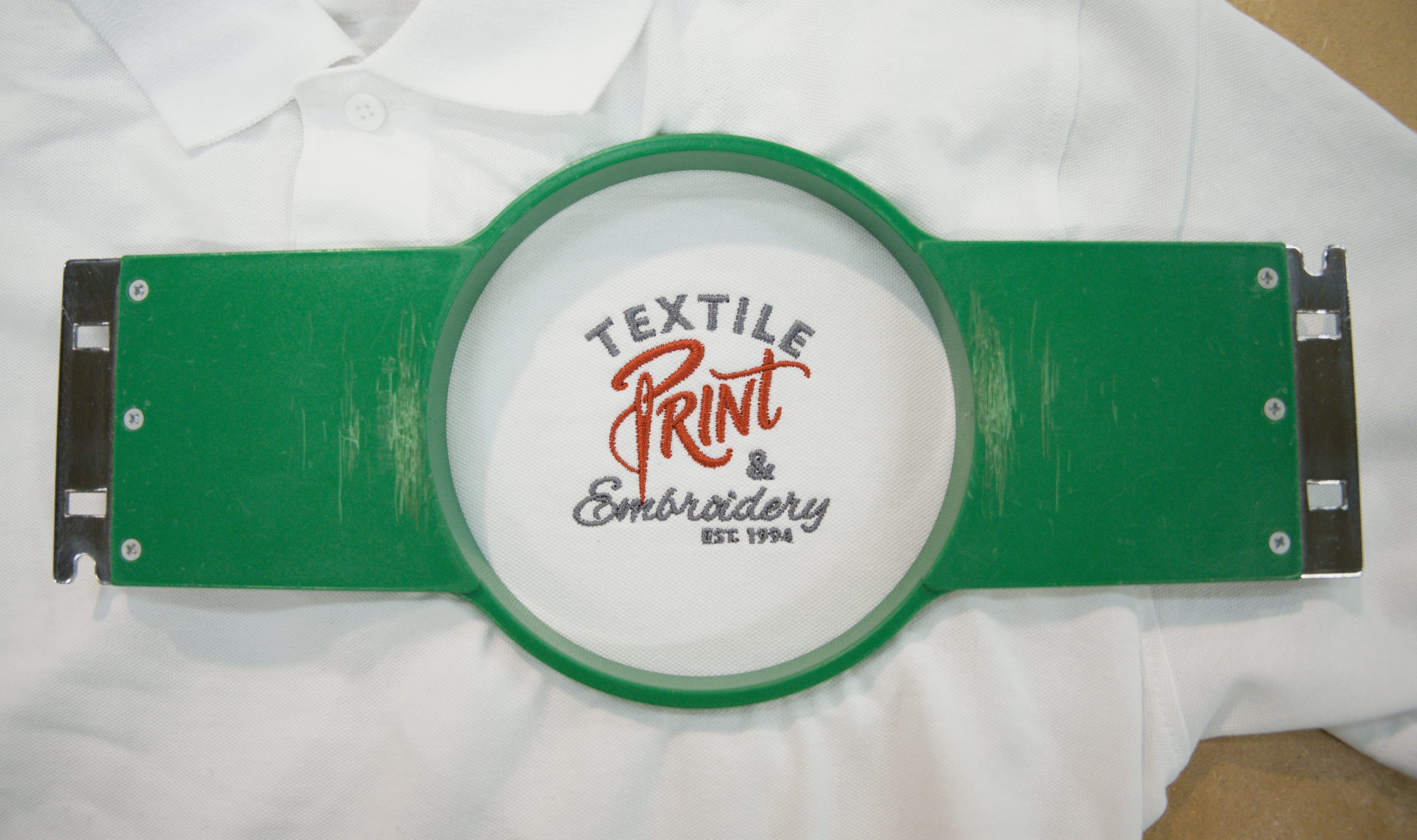 Textile Print and Embroidery logo embroidered on a white polo shirt, held in an embroidery hoop at our Limerick factory